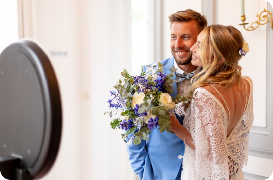 Un couple de jeunes mariés se prend en photo devant un photobooth mariage, borne photo, photomaton